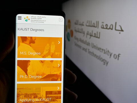 Stuttgart, Germany - 06-14-2025: Person holding cellphone with webpage of Saudi King Abdullah University (KAUST) on screen in front of logo. Focus on center of phone display.