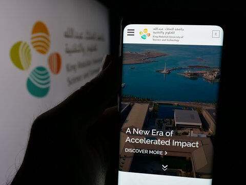 Stuttgart, Germany - 06-14-2025: Person holding smartphone with web page of Saudi King Abdullah University (KAUST) on screen in front of logo. Focus on center of phone display.