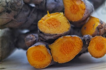 Close-up macro shot of freshly cut turmeric roots, showcasing the vibrant orange interior and rough exterior texture