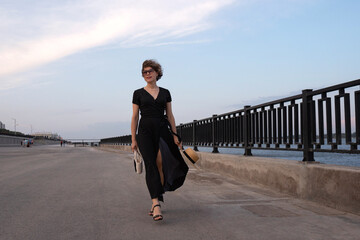 Woman in wrap dress walks by railing on urban seafront. A lady with beautiful long legs is wearing...