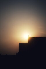 A silhouette of a rooftop with intricate details captured against the soft glow of a setting sun,...