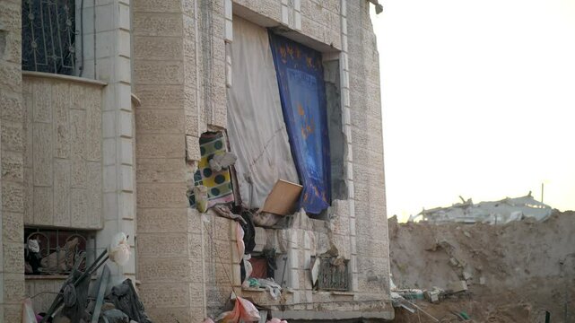 Facade of a bombed building in Gaza, where curtains, blankets, and fabric pieces are used to cover gaping holes and damage after destruction. Palestine