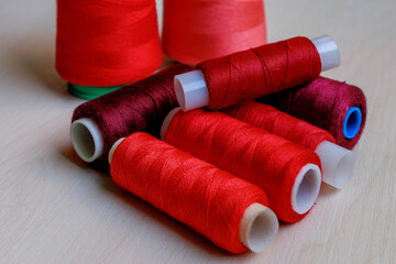 Colorful red and burgundy tailoring threads close-up on wooden background.