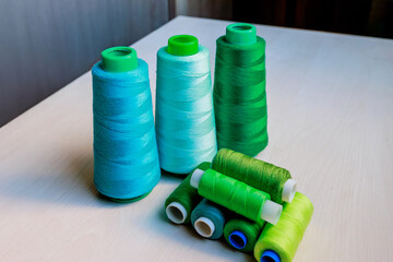 Colorful green and turquoise tailor's threads close-up on wooden background.