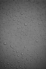 A detailed close-up black and white image of water droplets scattered on a smooth surface. The droplets create a clean and refreshing texture, emphasizing clarity and purity