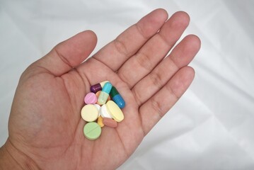 A close-up image of hands holding a variety of colorful pills and capsules, with a transparent bottle pouring the medication into the palm