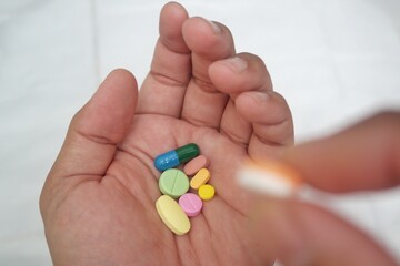 A close-up image of hands holding a variety of colorful pills and capsules
