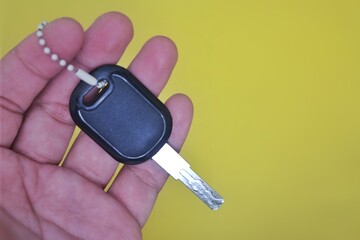 Hand Holding a Modern Car Key with Chain on Yellow Background