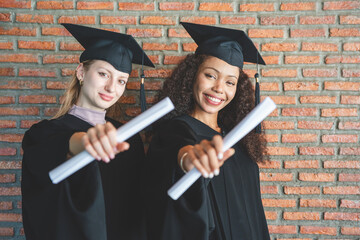 Two Smiling Female Students in Graduation Gowns, Happy Diverse Graduates Celebrating with Diplomas,...