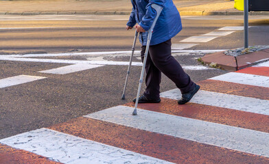 elderly person using crutches crossing a marked pedestrian crosswalk. Theme of accessibility and...