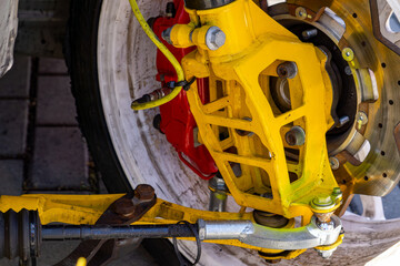 car suspension and disc brake system in a sports vehicle, featuring a yellow control arm, red brake...