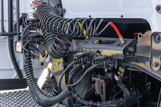 view of the rear cab area of a semi-truck, featuring coiled air hoses, electrical wiring, and trailer connection ports. Modern truck coupling system.