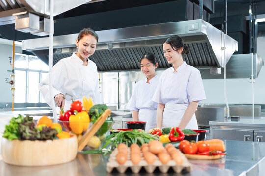 Professional Chefs and Students Learning in a Commercial Kitchen, Mentor Chef Guiding Young Aspiring Cooks, Healthy Cooking Workshop with Fresh Vegetables and Diverse Chefs