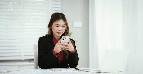 A young Asian businesswoman in a black blazer and red shirt calculates numbers on a white...