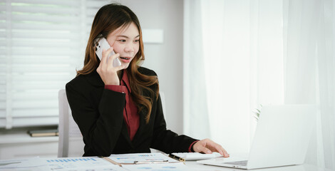 A young Asian businesswoman in a black blazer and red shirt calculates numbers on a white...