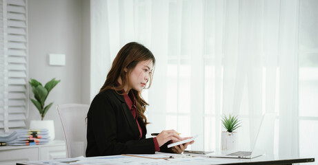 A young Asian businesswoman in a black blazer and red shirt calculates numbers on a white...
