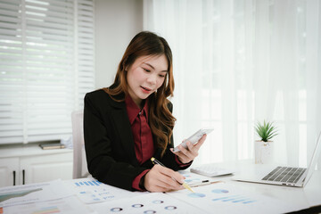 A young Asian businesswoman in a black blazer and red shirt calculates numbers on a white...