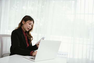 A young Asian businesswoman in a black blazer and red shirt calculates numbers on a white...