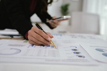 A businesswoman analyzes financial documents with charts and graphs at a desk, highlighting data...