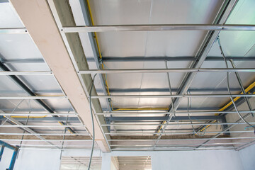 Interior renovation project showing new ceiling installation. An aluminium framework with complex electrical wiring hangs below unfinished slab showing sense of progress