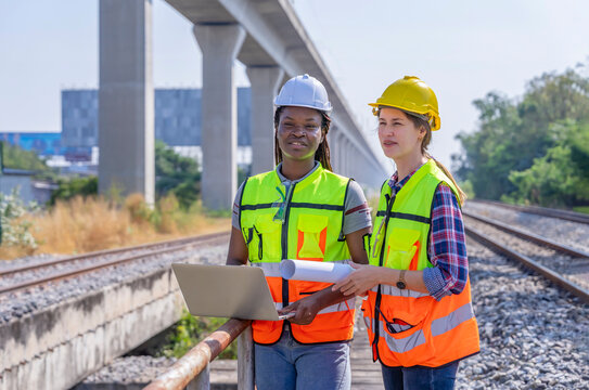 multiracial engineers inspecting at railway,african woman holding laptop and caucasian female holding blueprint,railway engineering,rail transportation