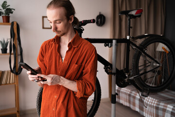 Young man repairing bicycle at home using smartphone to search for DIY repair info online