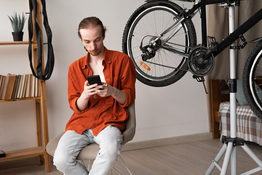 Young man repairing bicycle at home using online assistant for DIY bike maintenance and troubleshooting