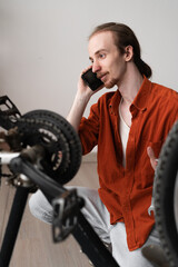 Young man calling bicycle repair service consulting mechanic on DIY bike maintenance at home