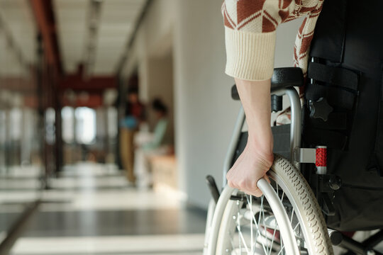 Close up of unrecognizable male hand gripping wheelchair wheel in modern coworking space, blurred people working in background
