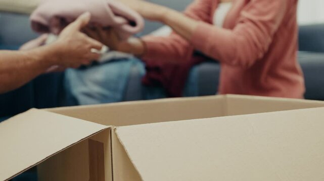 Close-up shot of adult hands placing a yellow sweater into a donation box at home. A caring gesture as part of a community support and charity effort.