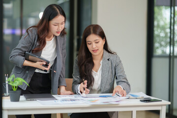 Two Asian businesswomen are sitting in a meeting, planning investment plans, business strategies. On the table are documents and graphs.	