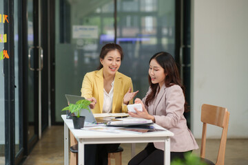 Two Asian businesswomen are sitting in a meeting, planning investment plans, business strategies. On the table are documents and graphs.	