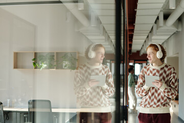 Young Caucasian man with red hair wearing patterned sweater and headphones standing in modern...