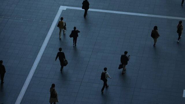 Aerial view of people walking on a tiled floor with strong shadows.