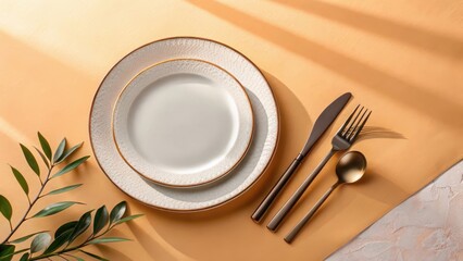 Minimalist table setup featuring ceramic plates, matte black cutlery, and soft natural light on a warm orange background with green leaves.