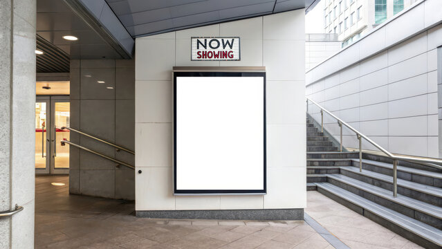 Empty lightbox movie poster frame beneath a Now Showing sign outside a modern cinema entrance, ready for upcoming film promotion.
