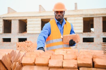 African american construction worker. Portrait of mason bricklayer installing red brick with trowel...