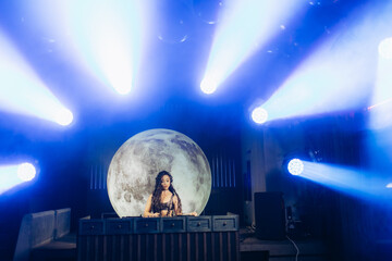 Female DJ Performing Under Dramatic Lighting and Full Moon Backdrop