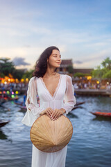Elegant Woman in White Dress Holding Traditional Hat in Hoi An, Vietnam