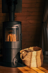 Cozy interior scene with a modern black wood-burning stove and a woven basket filled with firewood....