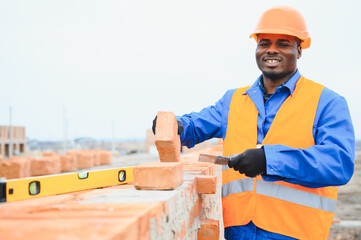 Builder in workwear and protective helmet keeping level handtool on surgace of brick layer while...