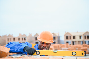 Builder in workwear and protective helmet keeping level handtool on surgace of brick layer while...