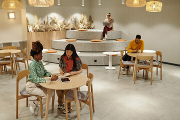 Black and Asian women collaborating at round table in modern coworking space, young adult men...