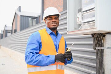 Joyful african american electrician mounting electric switchboard outdoors