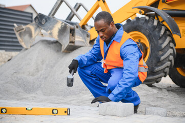 African american master in gloves lays paving stones in layers. Garden brick pathway paving by...