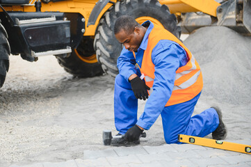 African american master in gloves lays paving stones in layers. Garden brick pathway paving by...