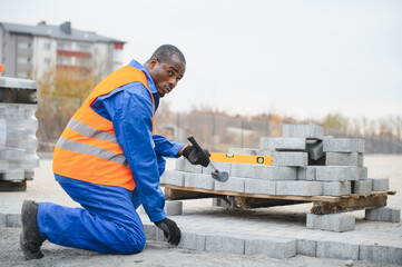 African american master in gloves lays paving stones in layers. Laying gray concrete paving slabs...