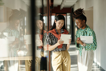 Young Asian woman and Black woman standing in modern coworking space, smiling and discussing...
