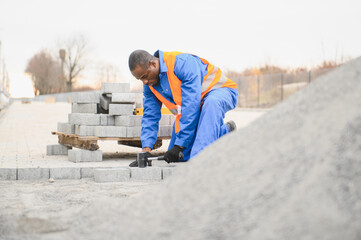 African american master in gloves lays paving stones in layers. Laying gray concrete paving slabs...