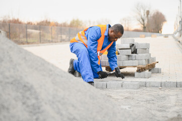 African american master in gloves lays paving stones in layers. Garden brick pathway paving by...